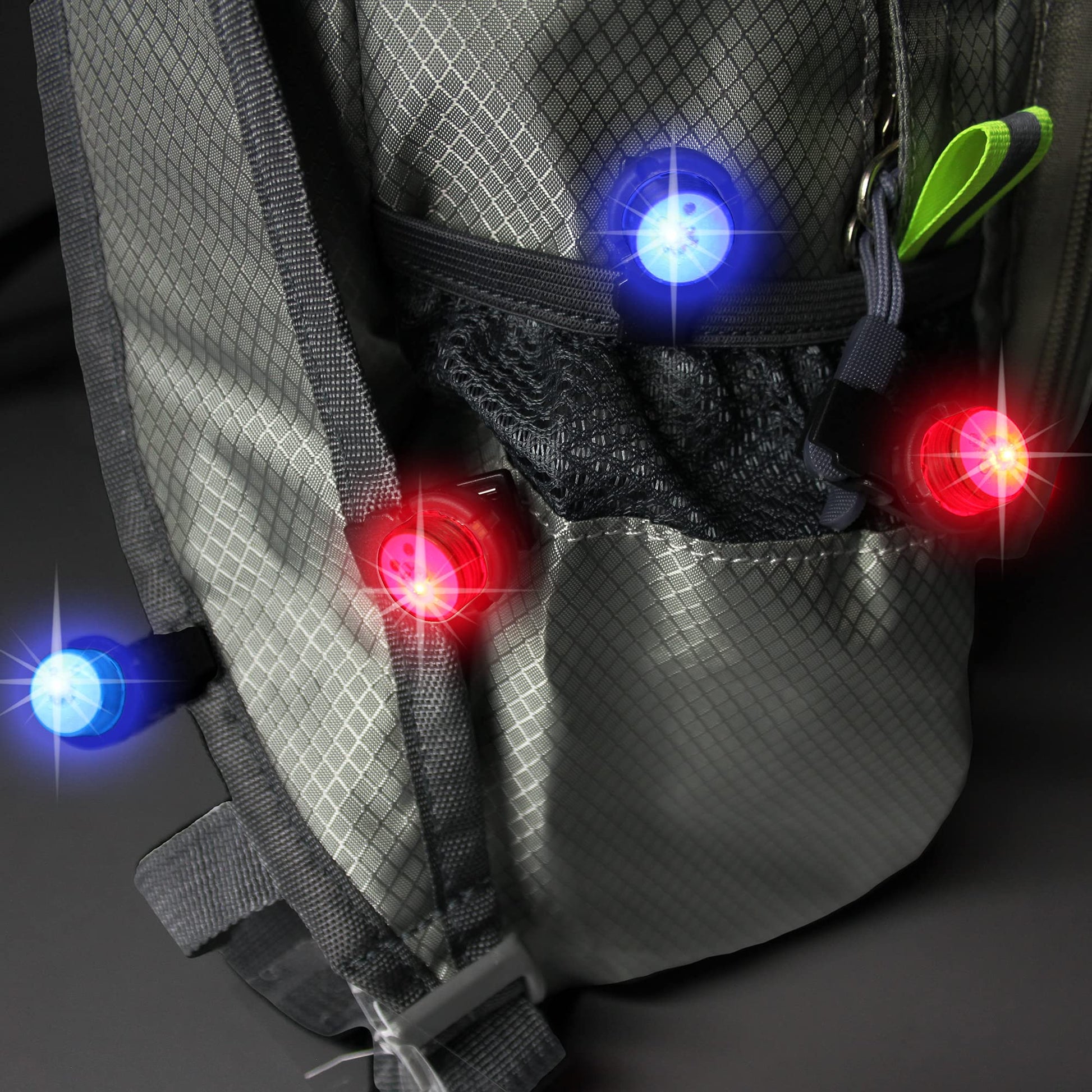 A photo of a grey backpack on a grey background with four WindNSun UFO Mini Lights flashing red and blue cliped along it's edges