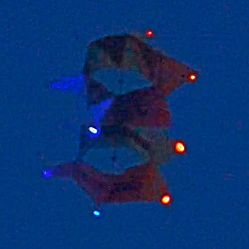 A dark grainy photo of a kite flying at night with the red and blue WindNSun UFO Mini Lights brightly illuminated while clipped to the edges of the kite