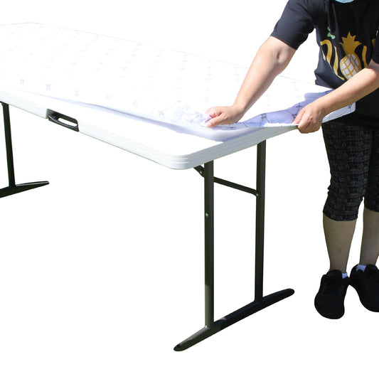 A person stretching TableCloth PLUS 72" Diamonds Polyester Tablecloth for 6' Folding Tables over a folding table
