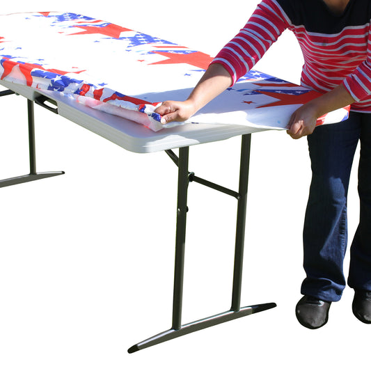 A person stretching TableCloth PLUS 72" Patriotic Fitted PEVA Vinyl Tablecloth for 6' Folding Tables over a folding table