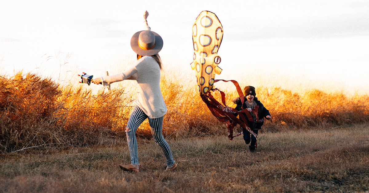 A parent and child flying colorful kites in a field at sunset